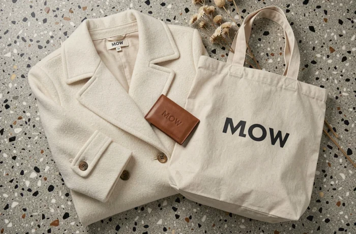Flat lay des produits de la marque MOW incluant manteau, porte-cartes et tote bag sur surface en terrazzo